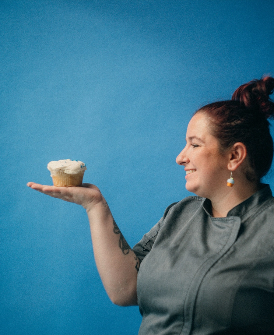Sam's Club bakery associate Bridgette Anderson holds a cupcake in the palm of her hand, standing against a blue background.