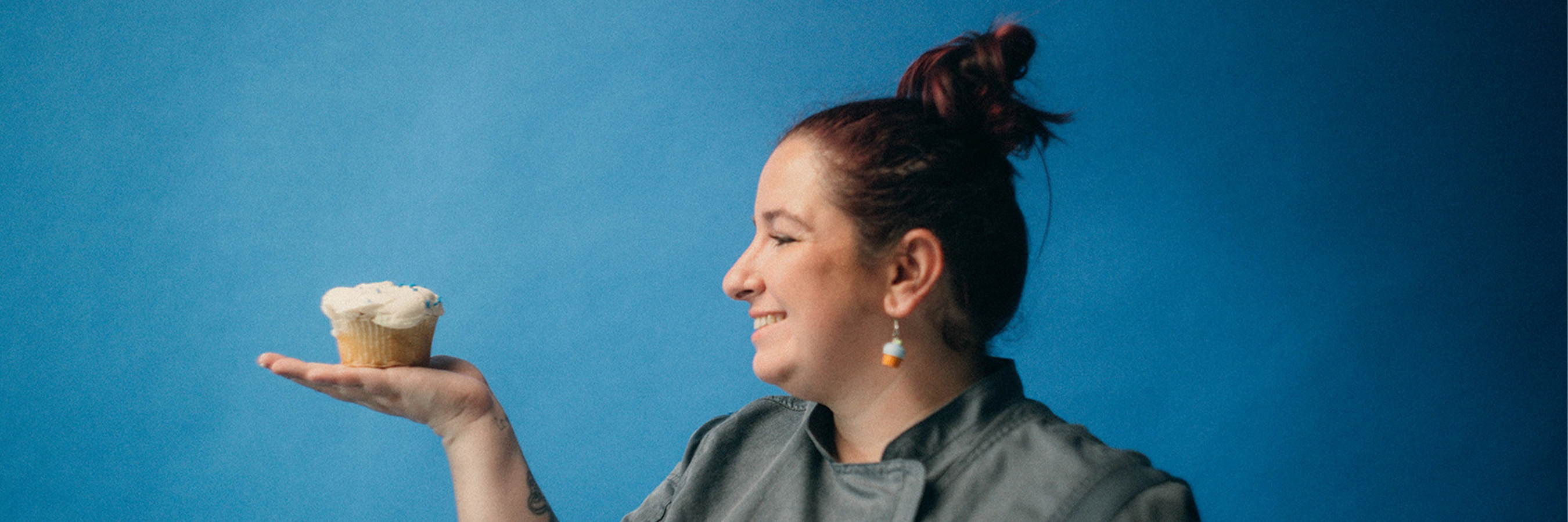 Sam's Club bakery associate Bridgette Anderson holds a cupcake in the palm of her hand, standing against a blue background.