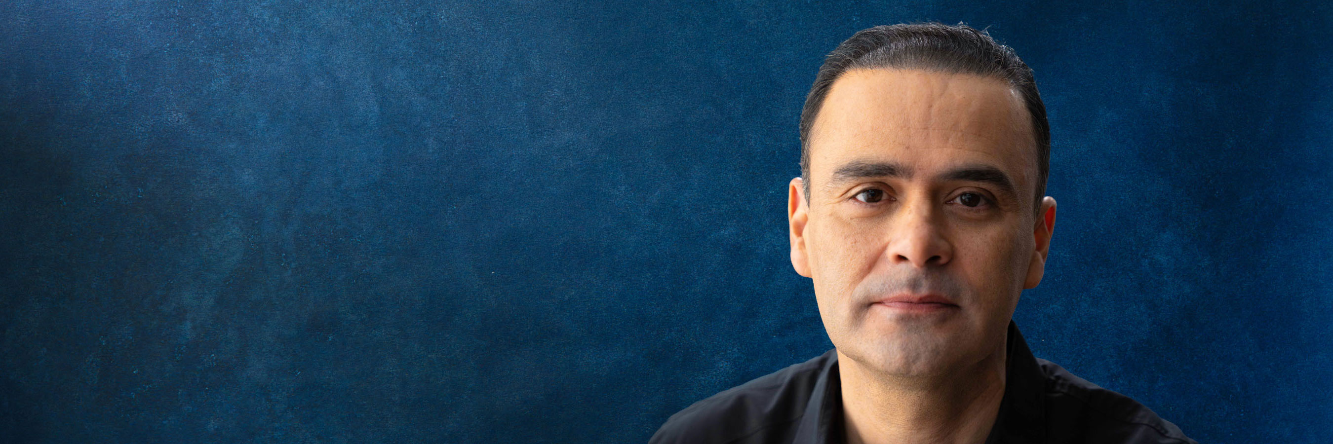 Close up photo of Oscar Romero standing against a dark blue background.