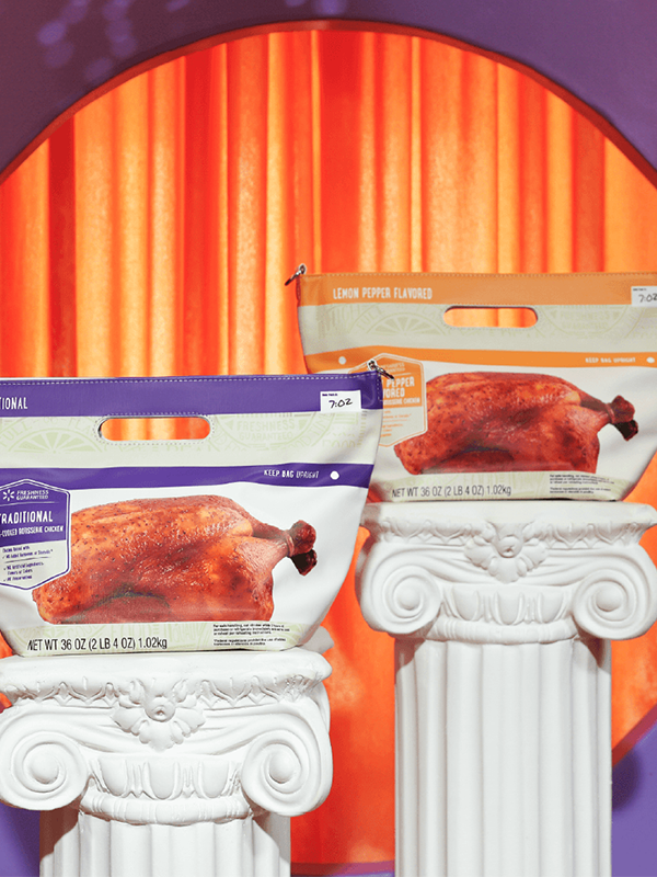 Two frozen turkey product bags are showcased on white classical-style pedestals. The bags feature roasted turkey imagery and are positioned in front of a circular orange curtain backdrop. The surrounding background is a smooth purple gradient, creating a bold contrast with the warm orange center. A small white rectangle with "5 lb" text is visible on the top right corner of each bag.