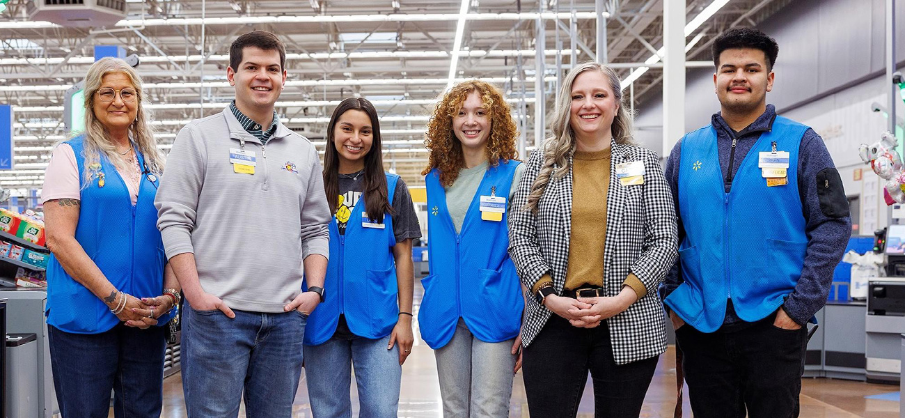 A group of Walmart associates smile together at the front of a store