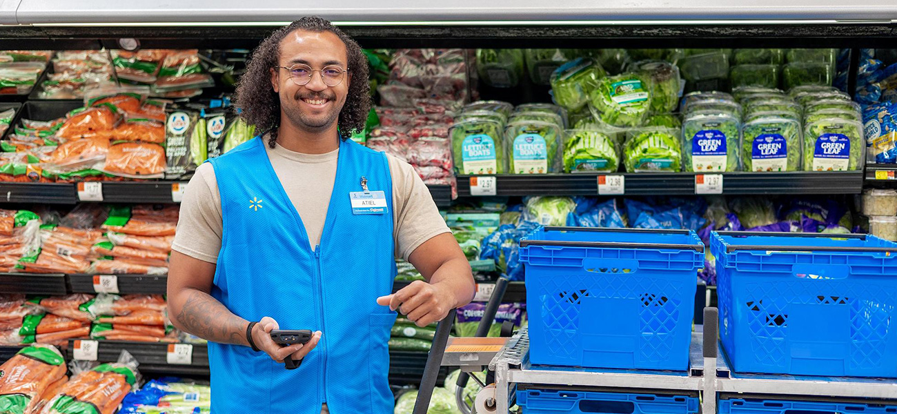 Walmart associate Atiel smiles in front of carrots in a Walmart store