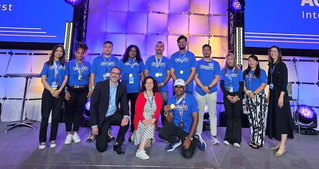 A group of individuals posing on stage during Associates Week 2025. The setting features visible text such as 'Integrity in Action Award' and 'Integrity Builds Trust.' The winners are dressed in blue shirts, with some wearing badges, and the mood is celebratory and professional.